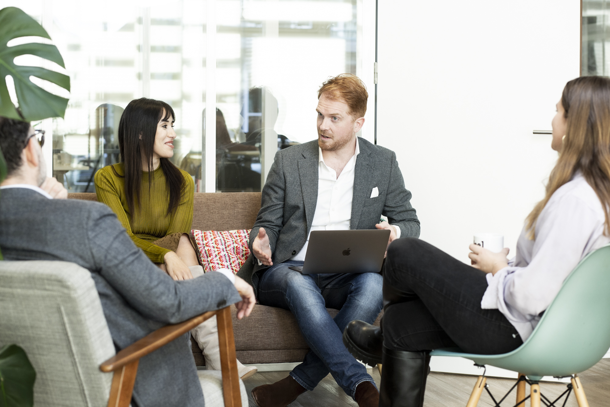 Chainels employee in smart casual clothing sitting on a sofa with laptop talking to colleagues